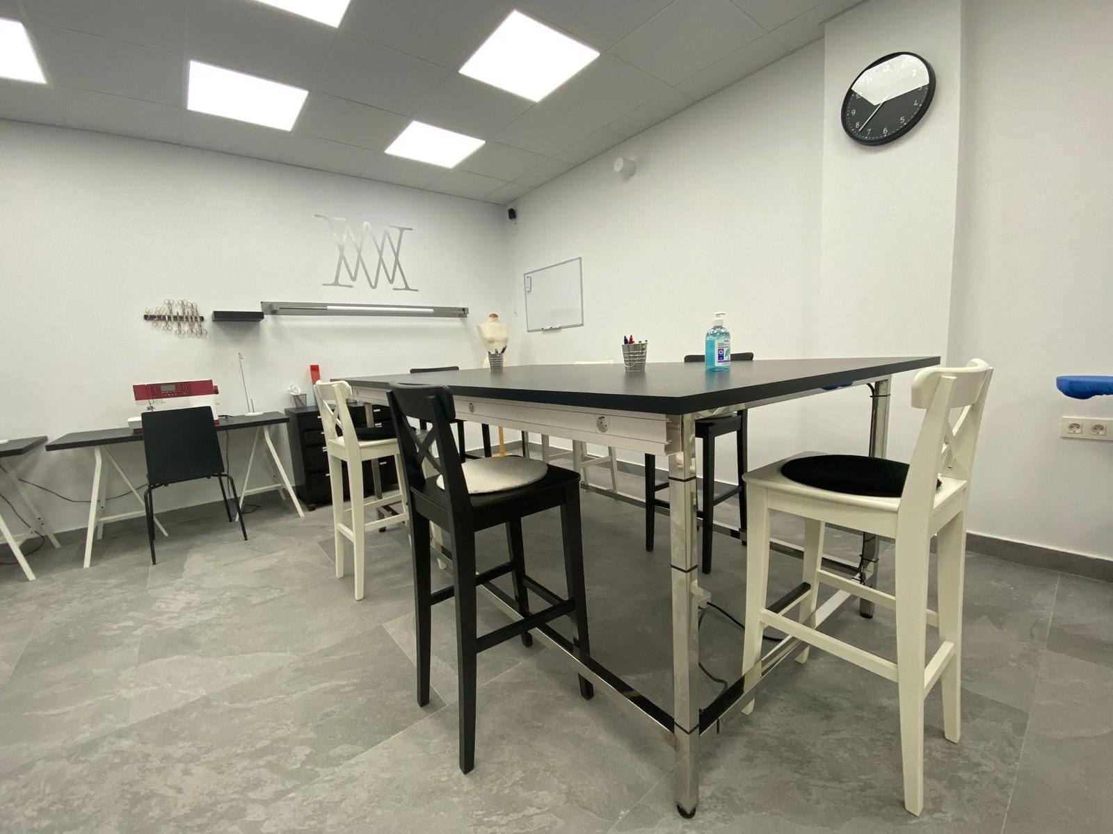 Aula amplia con mesas altas y sillas blancas y negras para clases de moda y diseño en Studio19
